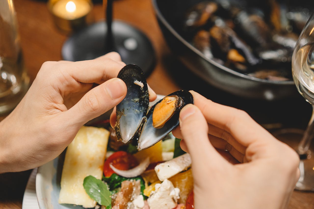 Mastering the First Impression: Your intriguing post title goes here Close-up of hands opening a mussel over a rich seafood dish, perfect for a gourmet dinner setting.